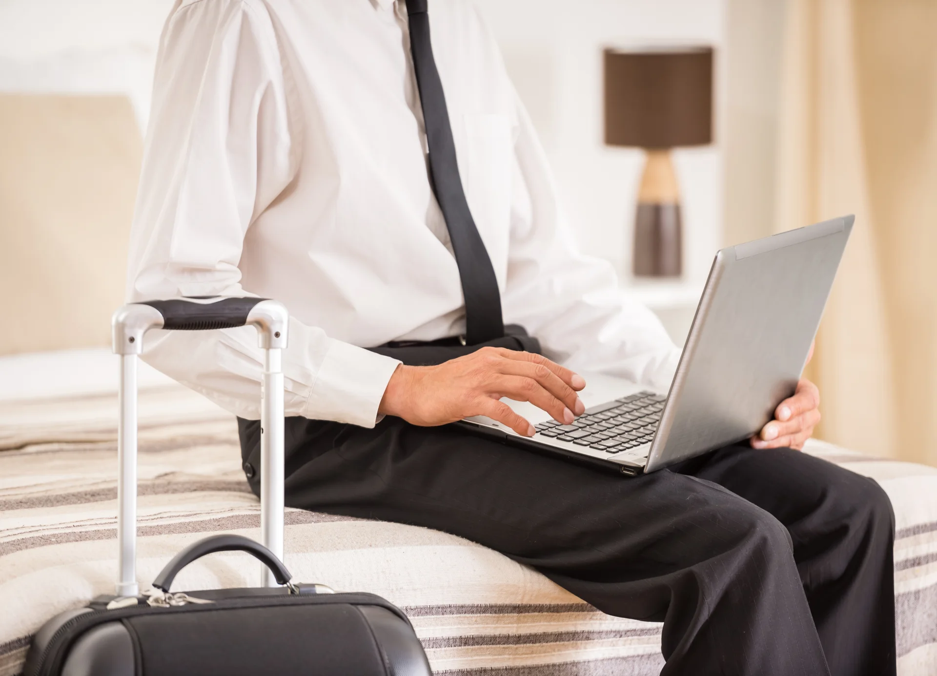 A traveller using a laptop while seated beside a suitcase
