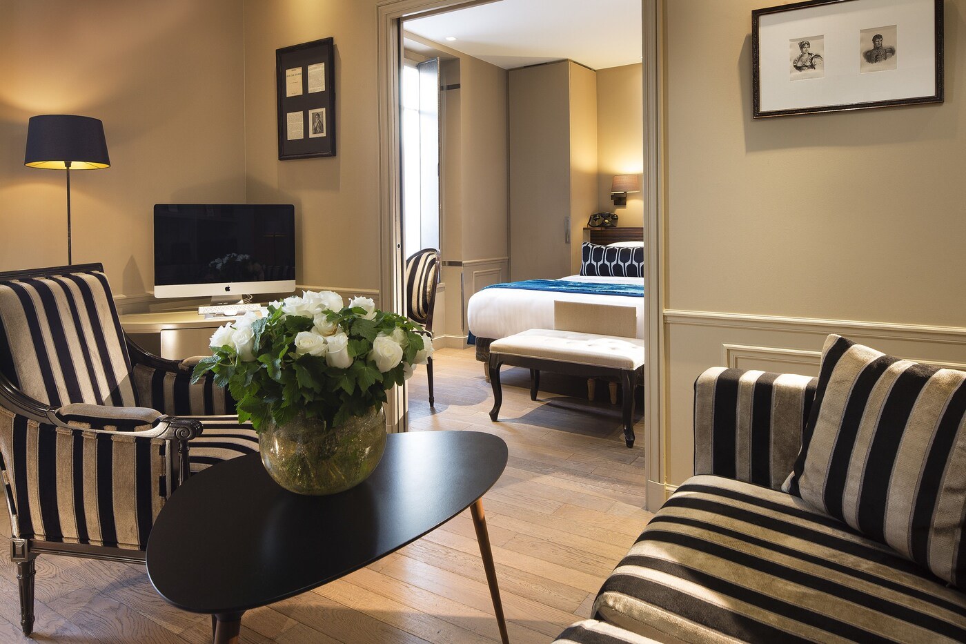 A hotel room with a striped sofa, a black table with a vase of flowers, a flat-screen TV, a bed with a striped duvet, and a framed picture on the wall. - Hotel & Spa La Belle Juliette (Paris)