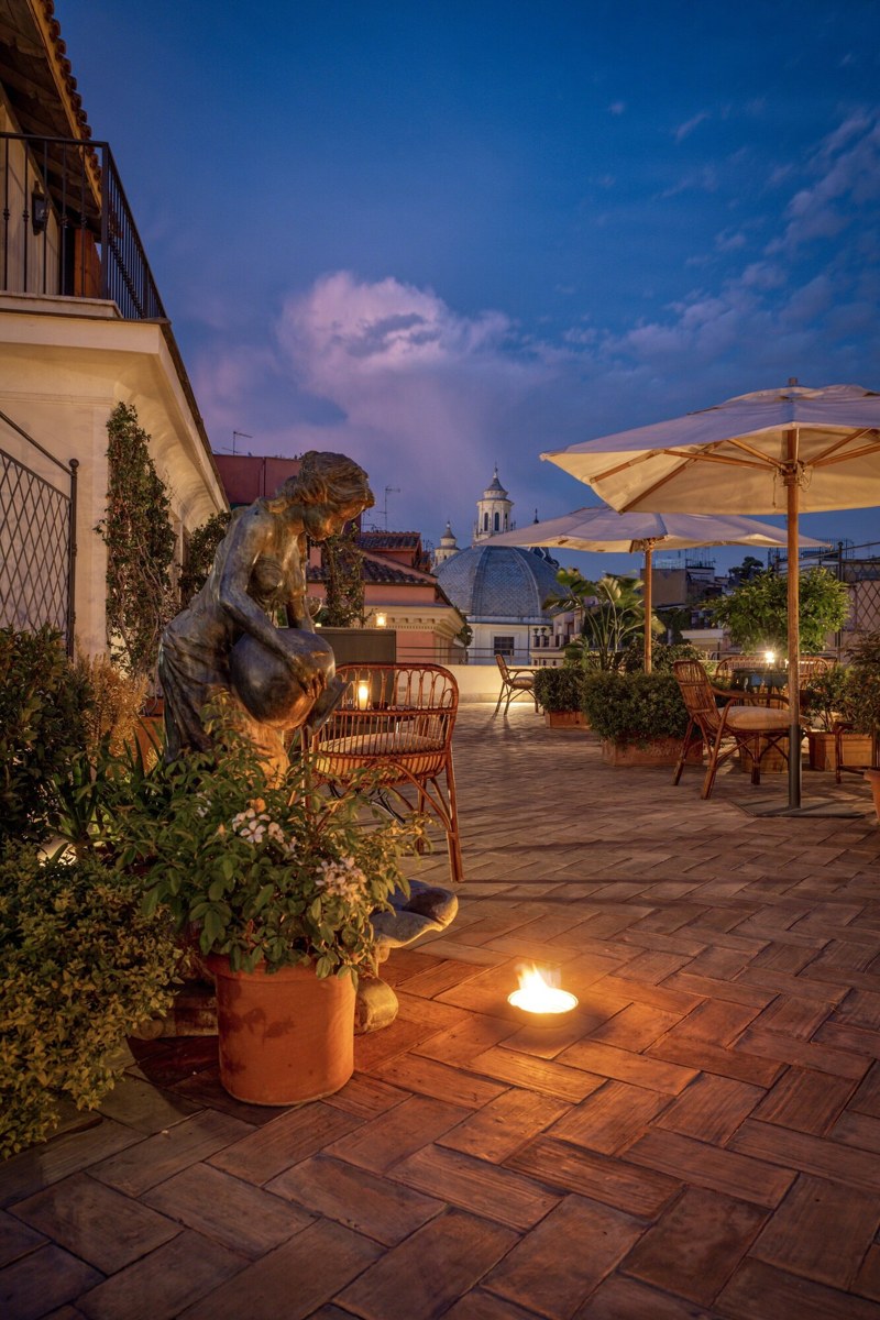 An outdoor patio with a statue, potted plants, and a table with chairs. - Hotel Locarno (Rome)