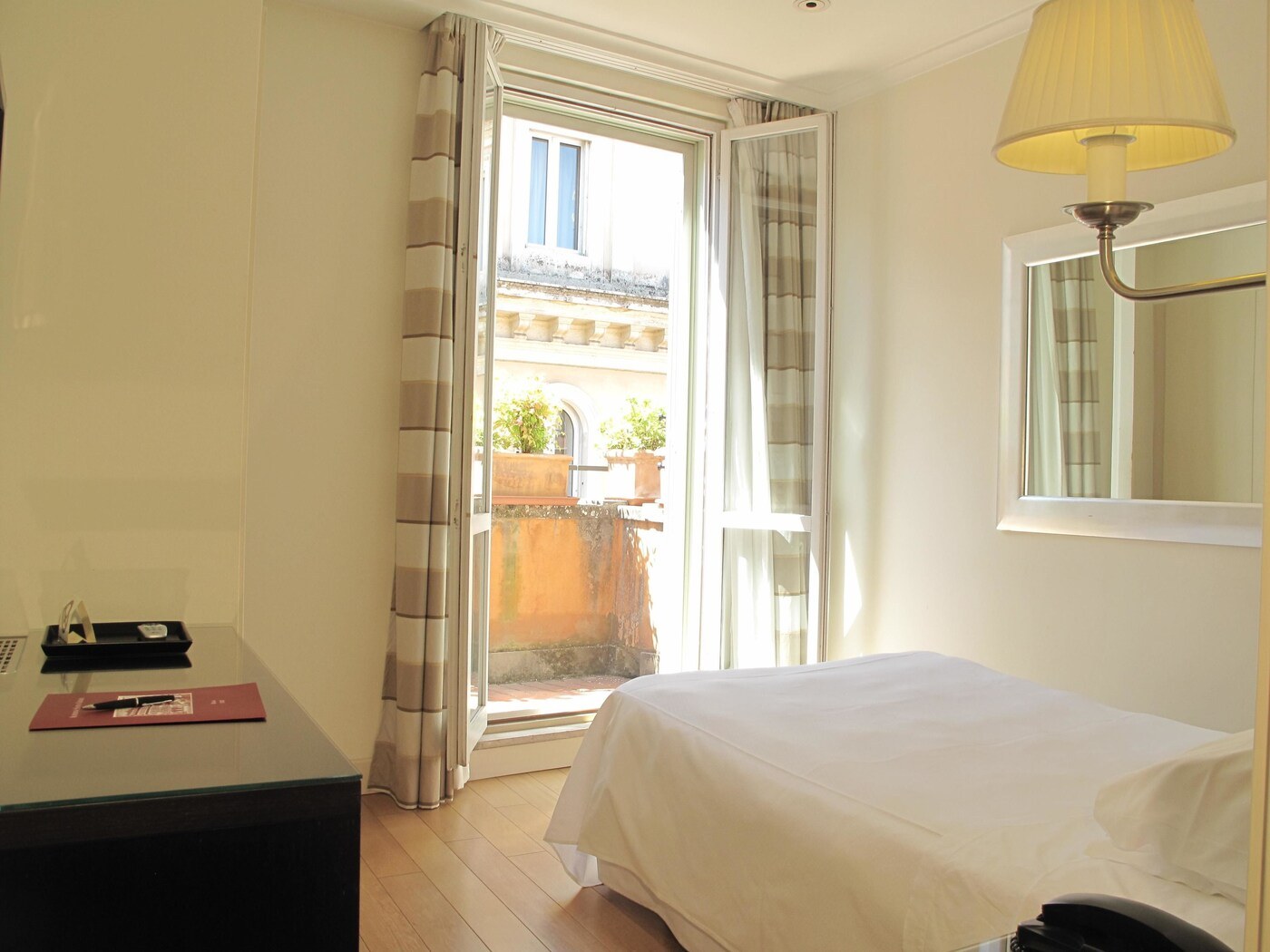 A hotel room with a bed, a desk, a lamp, and a view of the outside balcony. - Albergo Santa Chiara Hotel Rome (Rome)